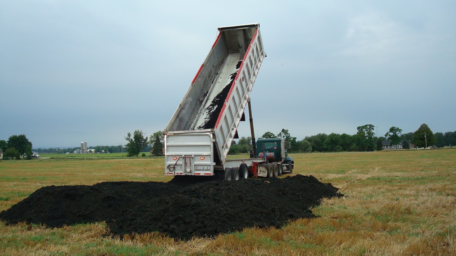 Biosolids truck dumping sludge Biosolids truck dumping biosludge on the land